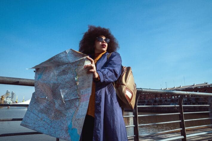 A Black woman with afro standing on a bridge with an opened map