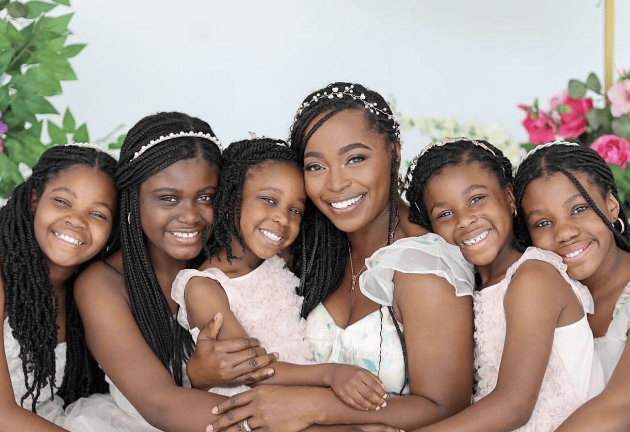 Black woman and five young girls smiling at the camera.