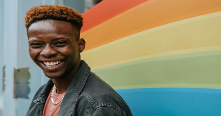 Positive young black guy laughing near graffiti wall with rainbow flag