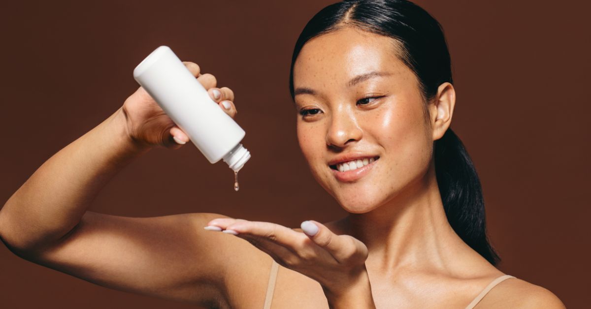 A woman pours a skin treatment serum out of a bottle towards her hands