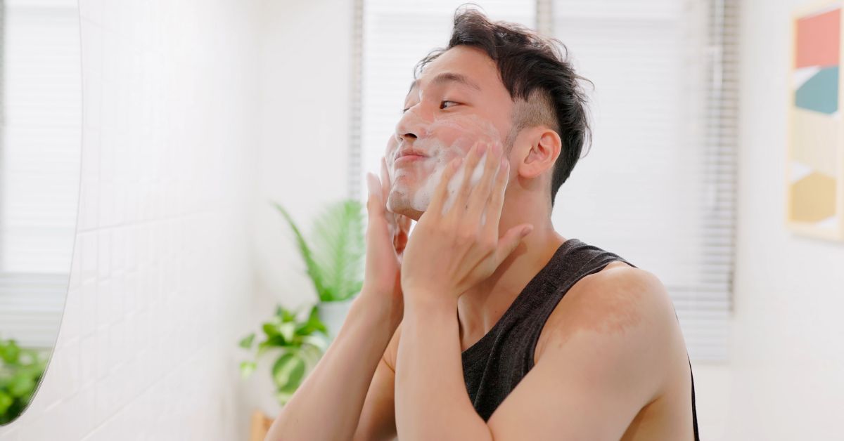 Man washing his face with a foamy cleanser looking at an off screen mirror