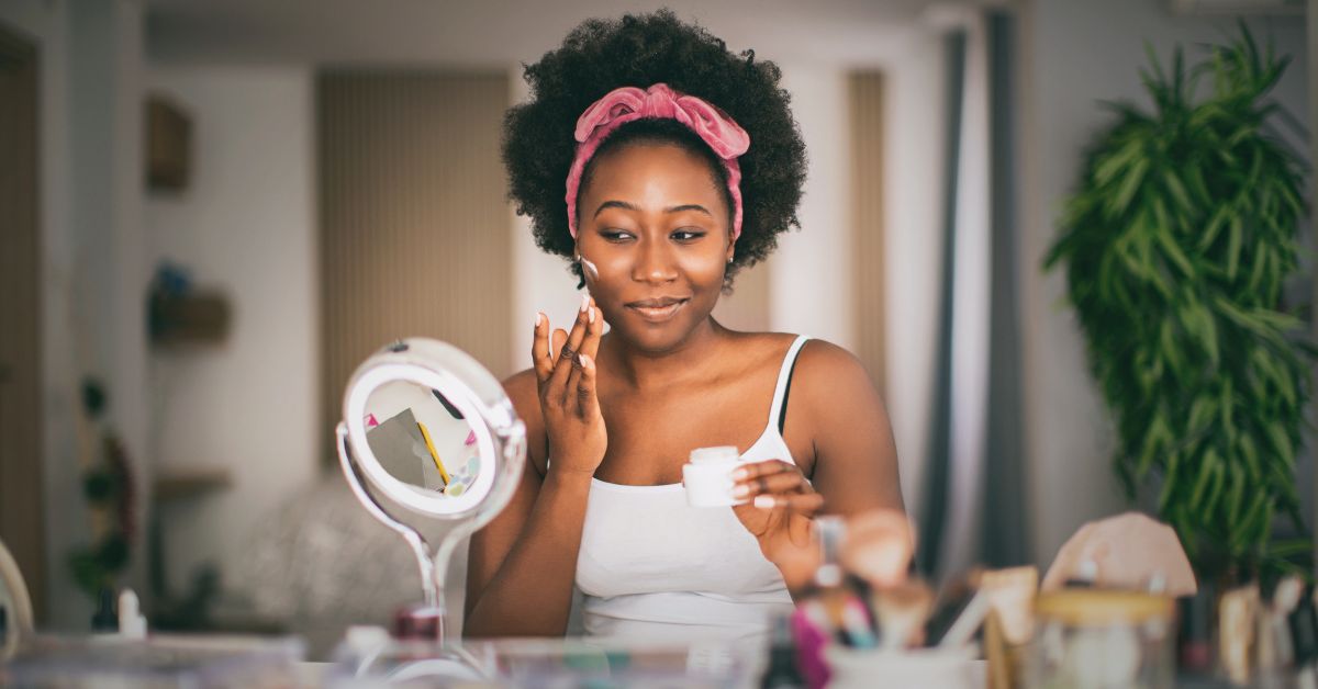 Woman sits at her vanity applying cream to her skin