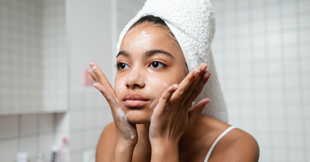 Woman with her hair wrapped up washing her face with both hands