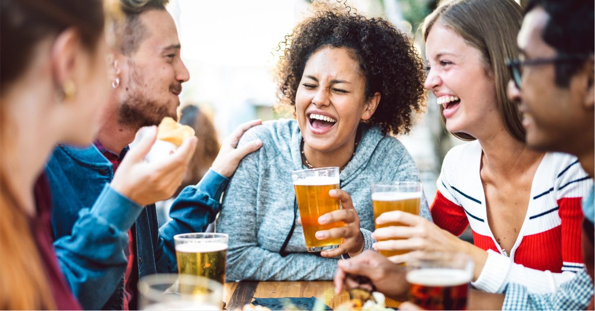 A multicultural group of friends laugh and drink beers at a restaurant (1)