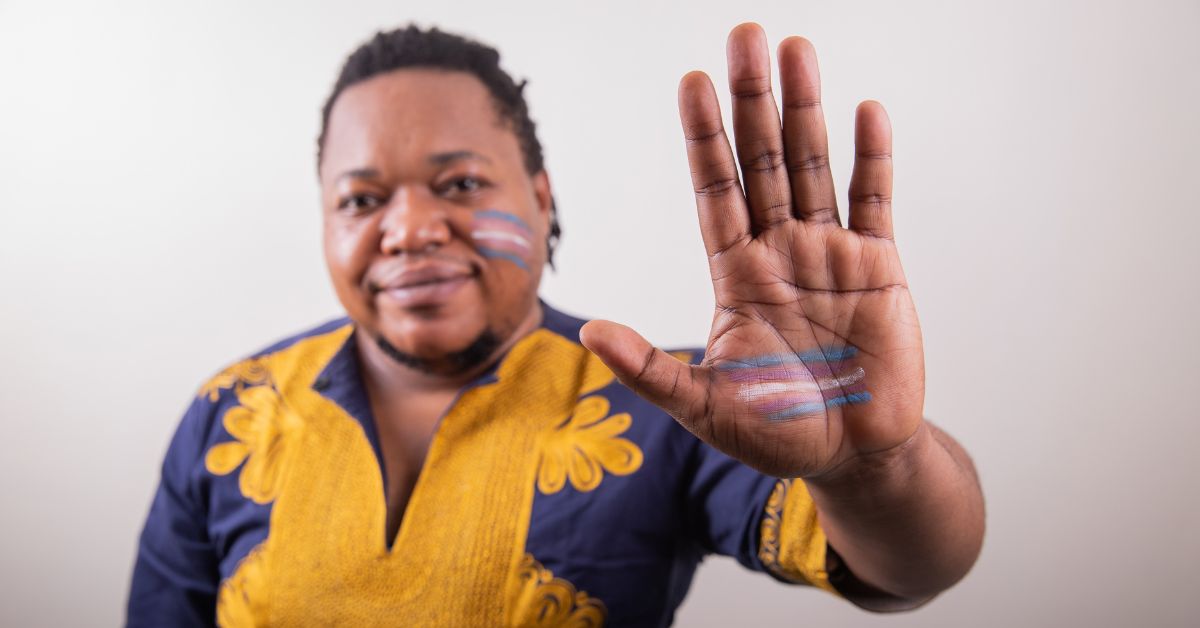 A trans man holds his hand up with the transgender flag painted onto his hand