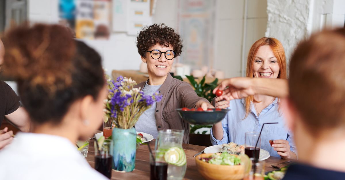 A woman passes a bowl of food across the table to another person at Friendsgiving