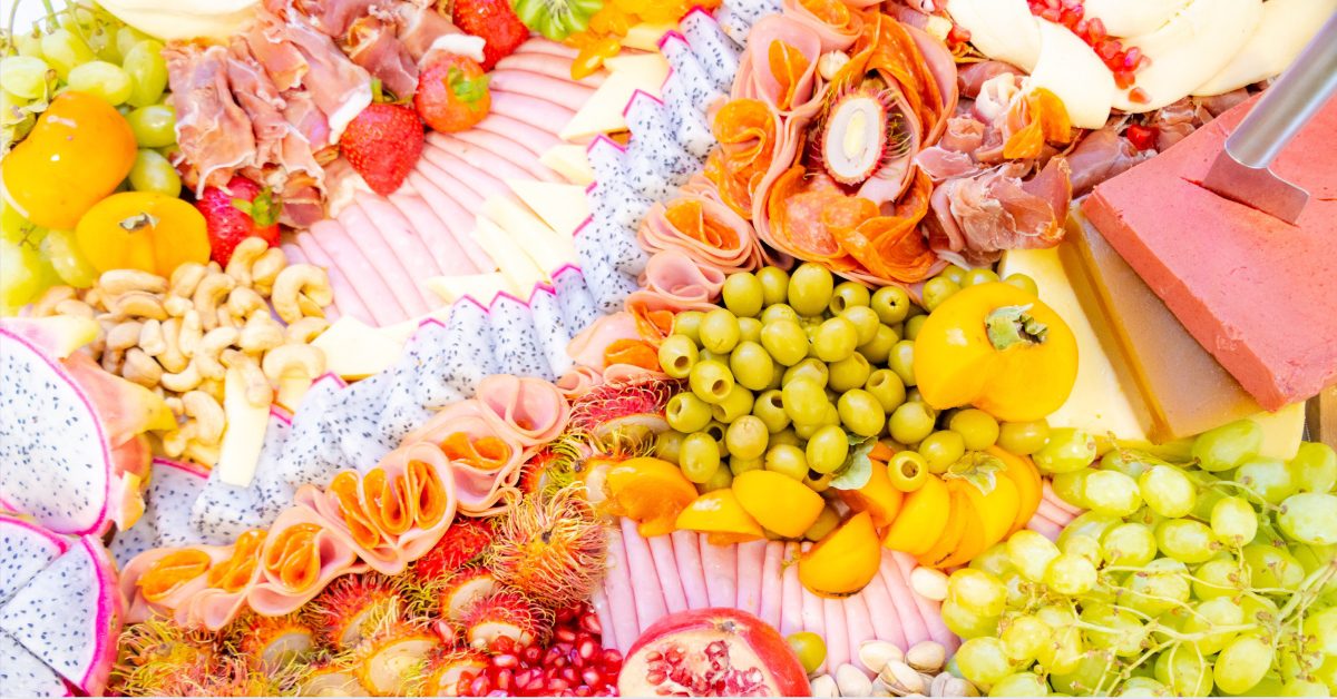 Charcuterie board filled with tropical fruits, meats, cheeses, and various olives and nuts (1)