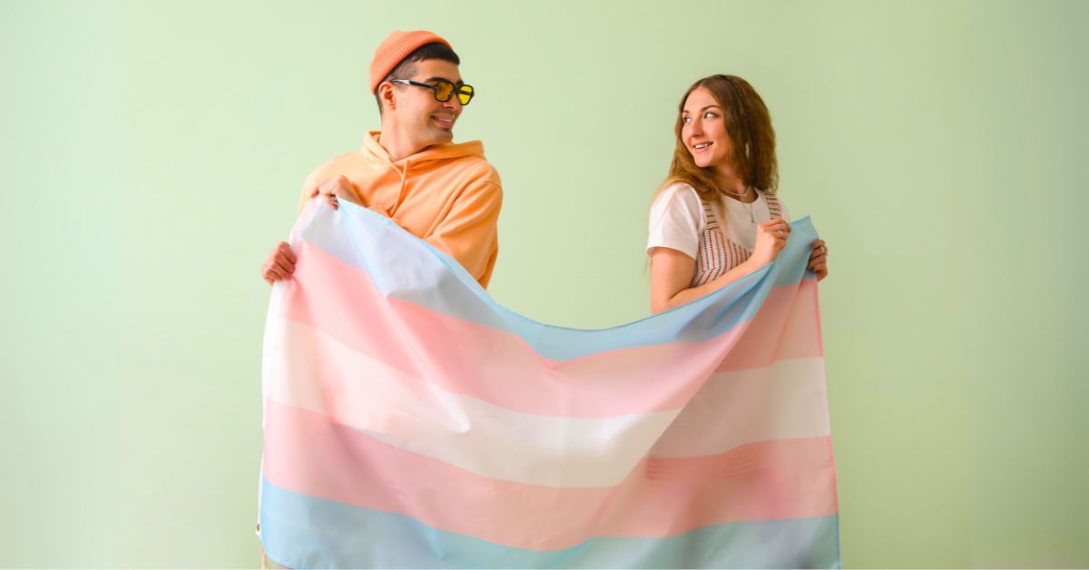 Two people looking over their shoulders as they hold one side of the Transgender flag in front of them